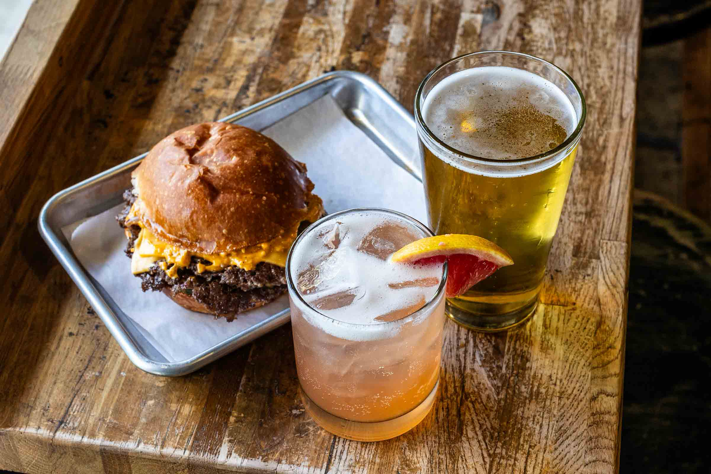 Sour Duck Market's smash burger and fries on a metal tray with a paloma and a beer
